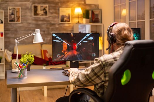 Back view of gamer male playing a shooter on his powerful PC computer late at night in the living room.