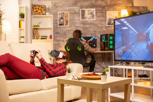 Woman lying on the sofa late at night in living room playing video games using a virtual reality headset