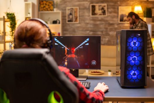 Back view of female gamer playing on powerful computer PC late at night in the living room.