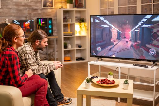 Couple playing video games on big screen TV in the living room late at night.