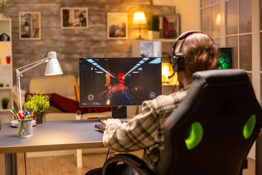 Back view of gamer male playing a shooter on his powerful PC computer late at night in the living room.