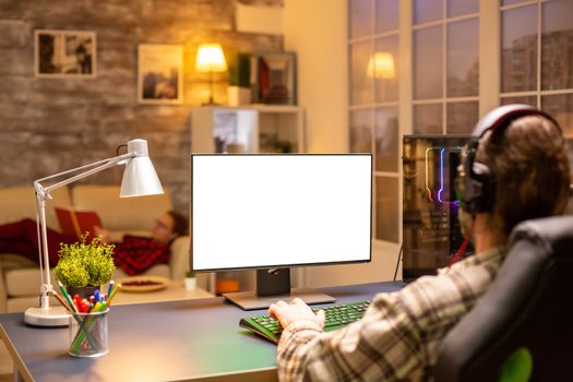 Back view of professional gamer looking at computer with isolated mock up screen late at night in the living room