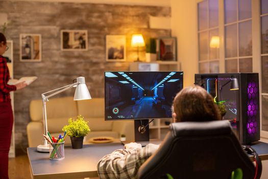 Back view of professional video gamer playing on powerful PC late at night in the living room.