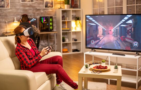 Woman gamer playing video games using a VR headset late at night in the living room