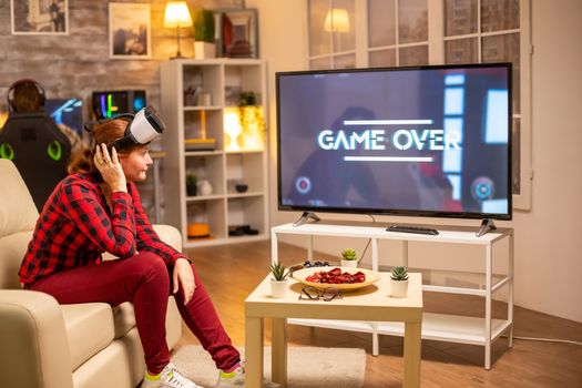 Woman losing at video games while playing using virtual reality headset late at night in the living room