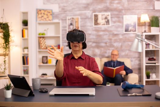 Old elderly woman using a VR virtual reality headset for the first time in her house. Concept of active elderly people using modern technology