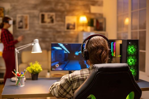 Back view of professional video gamer playing on powerful PC late at night in the living room.