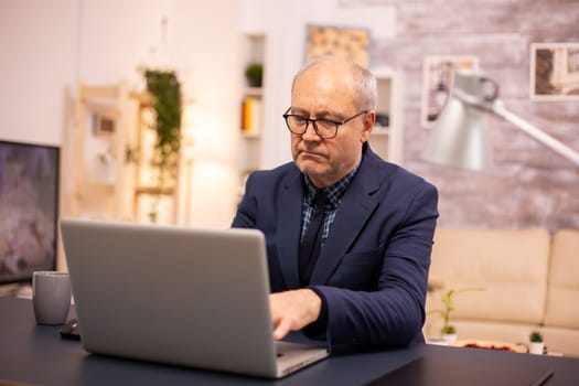 Elderly man typing on laptop in cozy living room.