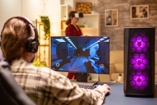 Back view of professional video gamer playing on powerful PC late at night in the living room.