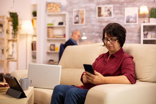 Elderly lady using modern technology in her house. She has a modern smartphone in her hands