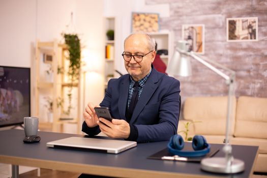 Old man using new technology in cozy house. He has a smartphone in his hands