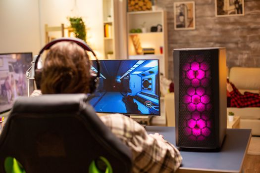 Back view of gamer male playing a shooter on his powerful PC computer late at night in the living room.