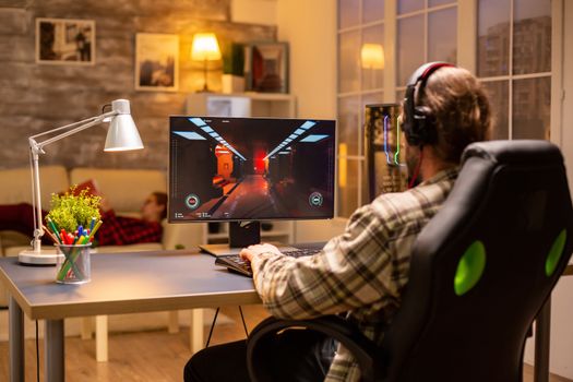 Back view of gamer male playing a shooter on his powerful PC computer late at night in the living room.