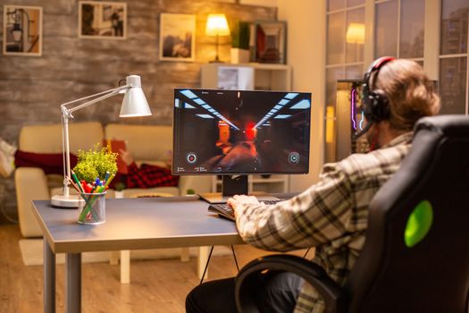 Back view of gamer male playing a shooter on his powerful PC computer late at night in the living room.