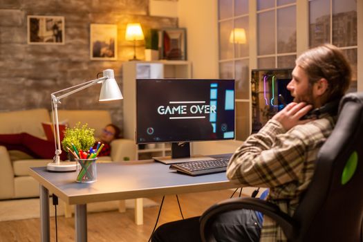 Back view of gamer male playing a shooter on his powerful PC computer late at night in the living room.