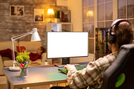 Back view of professional gamer looking at computer with isolated mock up screen late at night in the living room