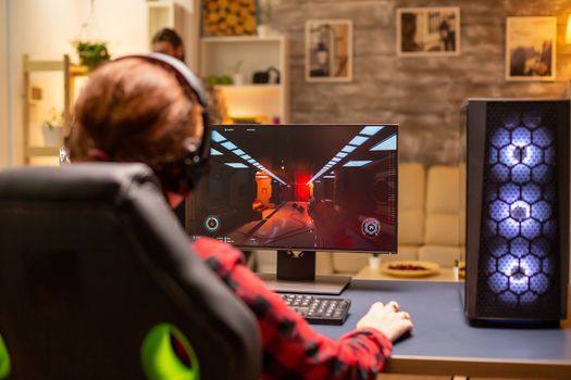 Back view of female gamer playing on powerful computer PC late at night in the living room.