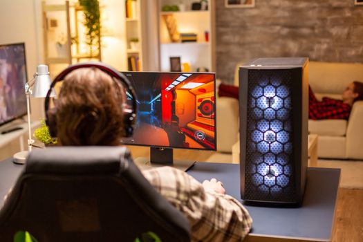 Back view of gamer male playing a shooter on his powerful PC computer late at night in the living room.