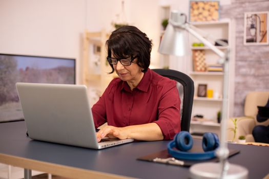 Old woman using a modern computer in her living room while her husband walks in the background