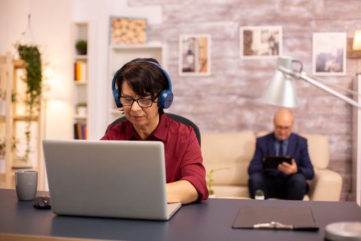 Concept photo of old lady using modern technology. He uses wirelles headphones and a laptop