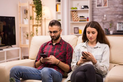 Boyfriend and girlfriend using their phones while sitting together on couch.