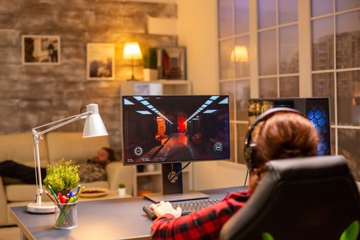 Back view of female gamer playing on powerful computer PC late at night in the living room.