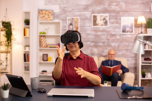 Old elderly woman using a VR virtual reality headset for the first time in her house. Concept of active elderly people using modern technology