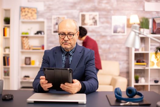 Senior man in his 60s using a modern digital tablet in his cozy home