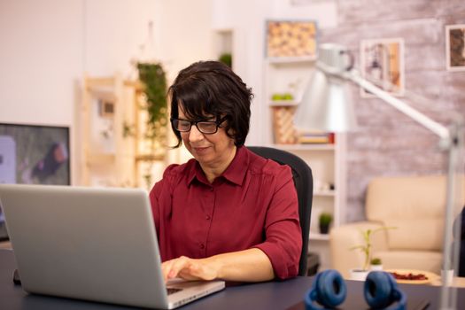 Old woman using a modern computer in her living room while her husband walks in the background