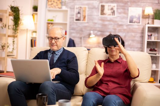 Old elderly retired woman in her 60s experiencing virtual reality for the first time in their cozy apartment