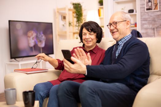 Old eldelry couple using a smartphone to talk with their family.