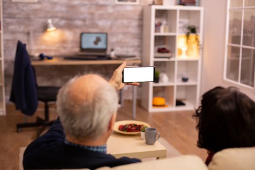 Back view of elderly retired couple looking at a smartphone with white isolated screen.