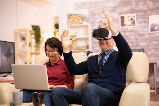 Old elderly retired man using VR virtual reality headset in their cozy apartment.