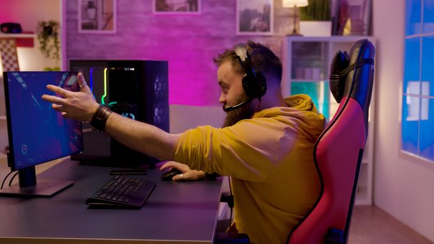 Excited professional game player sitting on a gaming chair in a room with colorful neon lights.