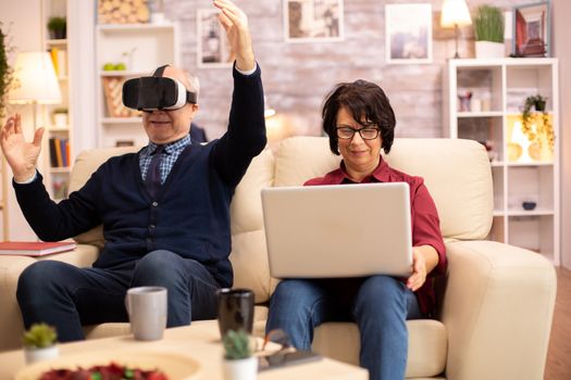 Old elderly retired man using VR virtual reality headset in their cozy apartment.