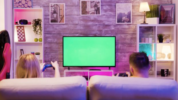 Young couple sitting on sofa and playing online games on tv with green screen. Happy relationship. Gamers couple.