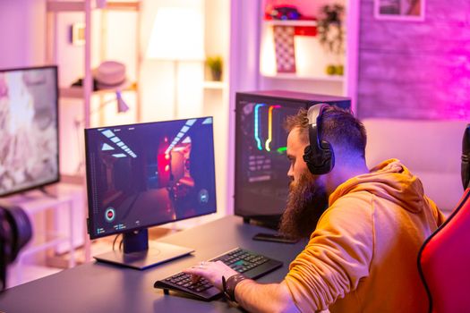 Hipster man playing professional video games in his room with colorful neons. Man wearing headphones while playing video games.