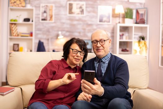 Beautiful elderly couple taking a selfie while sitting on the couch in the living room