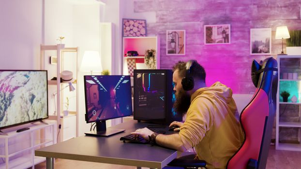 Successful man playing online video games in a room with colorful neons. Man sitting on gaming chair.