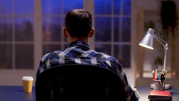 Back view of film editor working from home office at night hours.