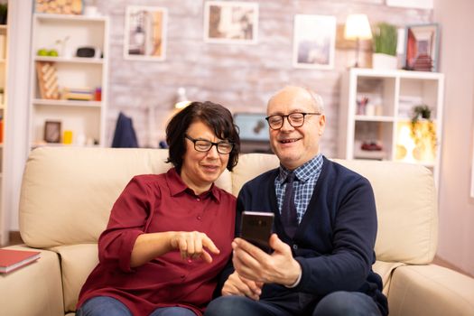 Beautiful elderly couple taking a selfie while sitting on the couch in the living room