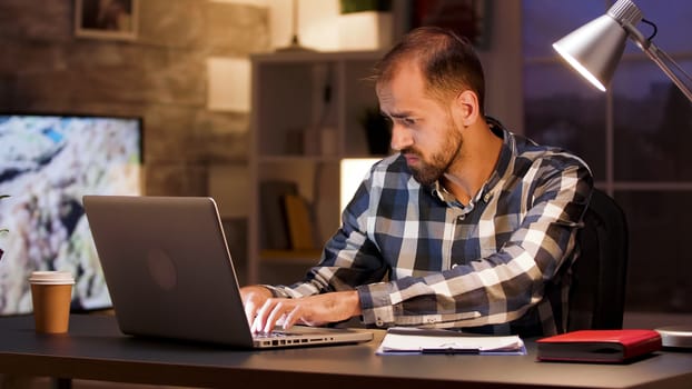 Businessman typing on laptop and searching through documents while working from home office.