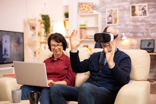 Old elderly retired man using VR virtual reality headset in their cozy apartment.