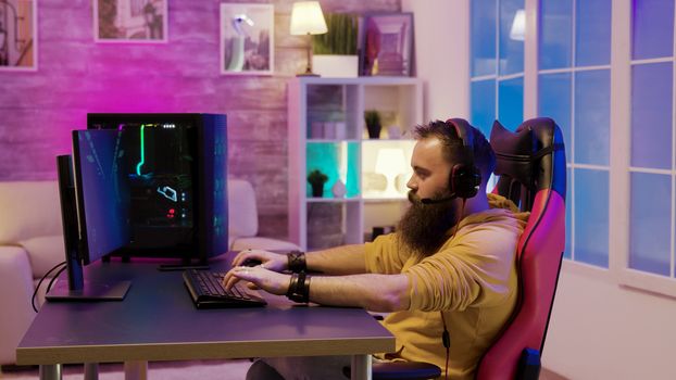 Bearded man playing video games in a room with colorful neons. Man talking with his friends while playing video games.