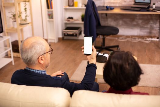 Back view of elderly retired couple looking at a smartphone with white isolated screen.