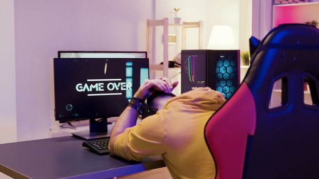 Man in a room with colorful neon lights sitting on gaming chair and playing professional online games.