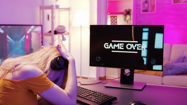 Blonde girl upset she lost on a shooter online game. Game over for player girl. Girl sitting on gaming chair.