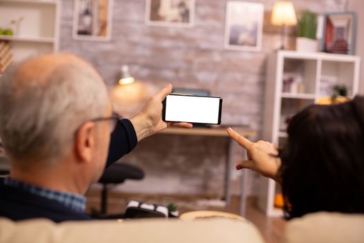 Back view of elderly retired couple looking at a smartphone with white isolated screen.