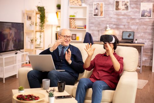 Old elderly retired woman in her 60s experiencing virtual reality for the first time in their cozy apartment
