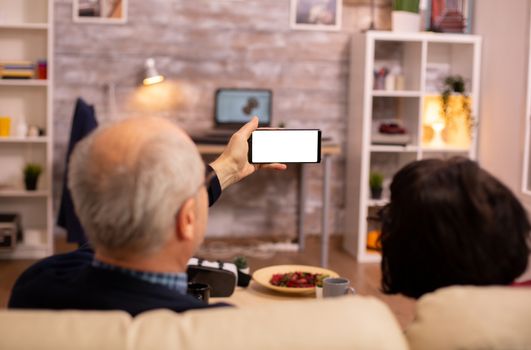 Back view of elderly retired couple looking at a smartphone with white isolated screen.